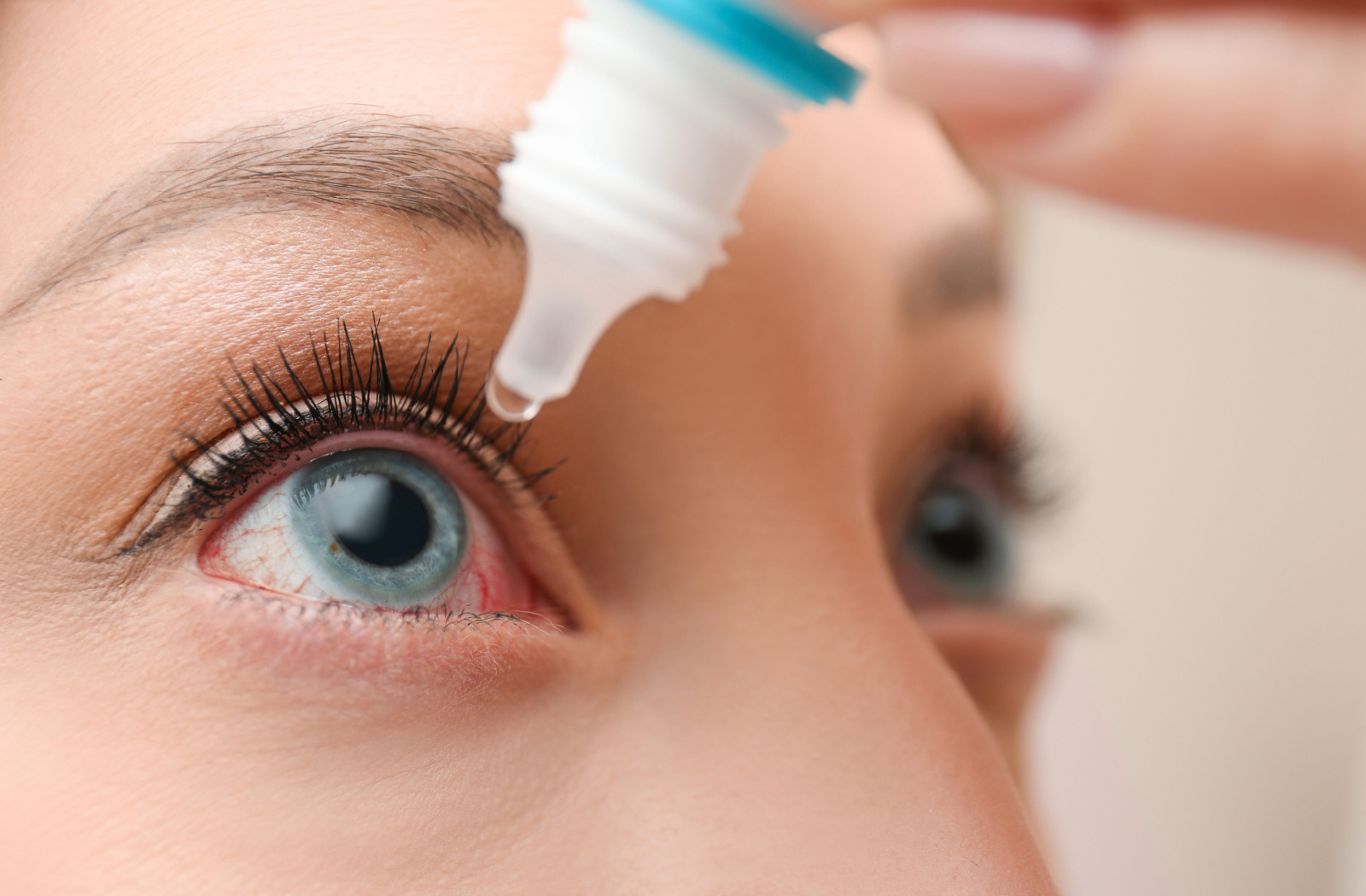 A close up of a woman putting eye drops in her eye.