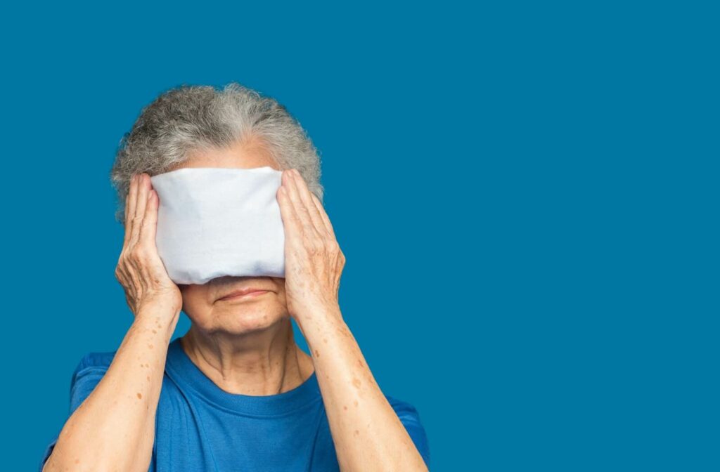 Against a blue backdrop, a senior holds a warm compress against their eyes and nose to find relief from styes