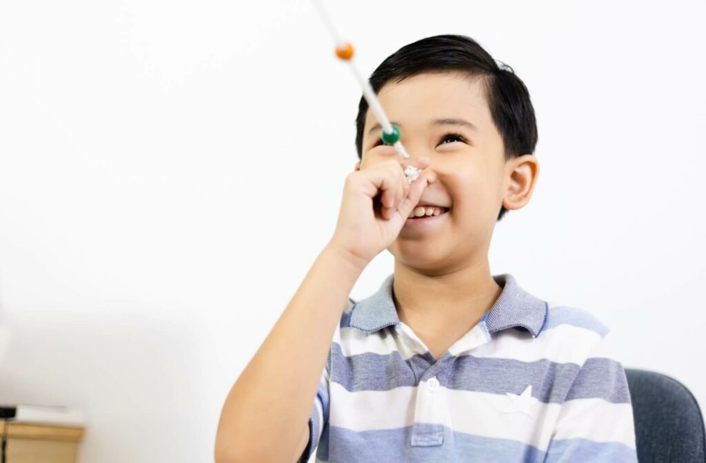 A smiling child performs a vision therapy exercise using a white rope and coloured beads.